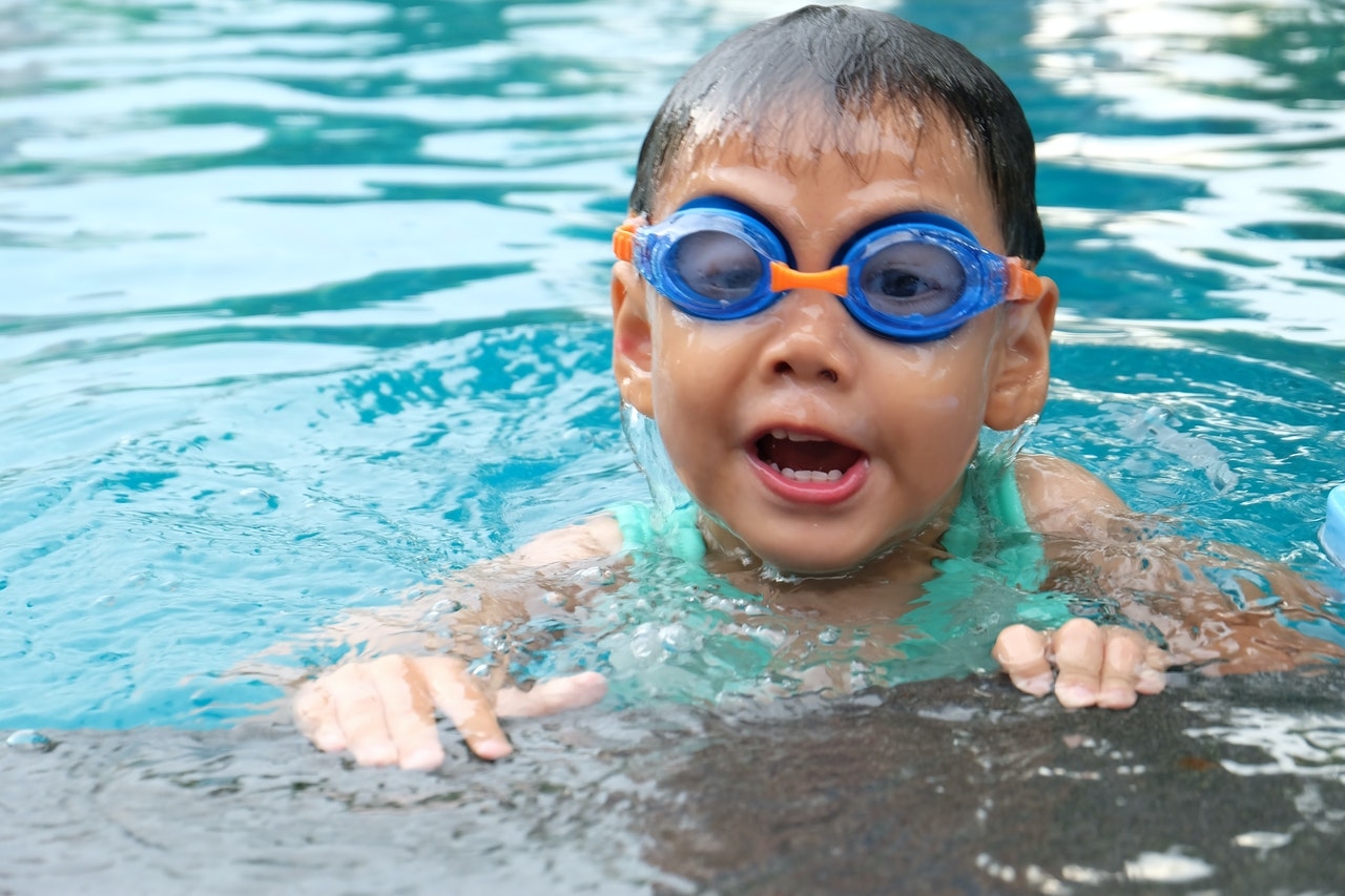 Bambino che nuota in piscina con gli occhialini blu