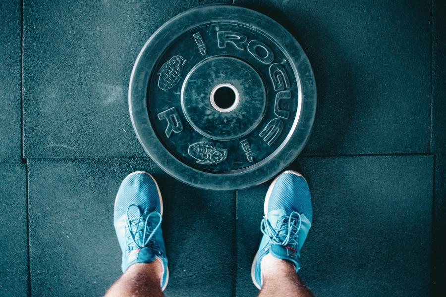 dark matt floor with a man standing in blue snickers and a gym plate laying in front of him