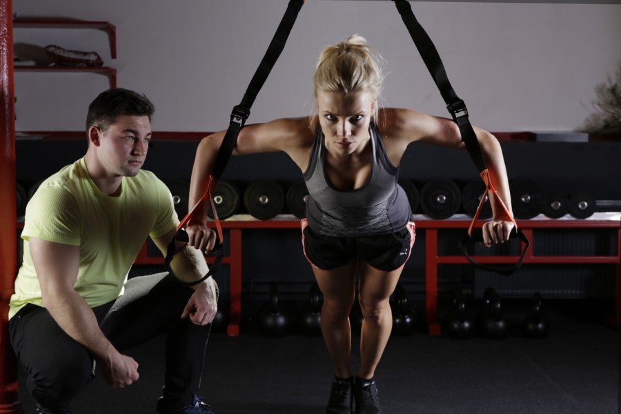 a woman exercising at a gym assisted by a trainer