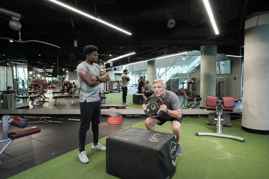 man doing squats in a gym with a trainer