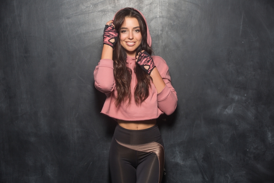 smiling brunette in pink hoodie and gym leggings on black background 