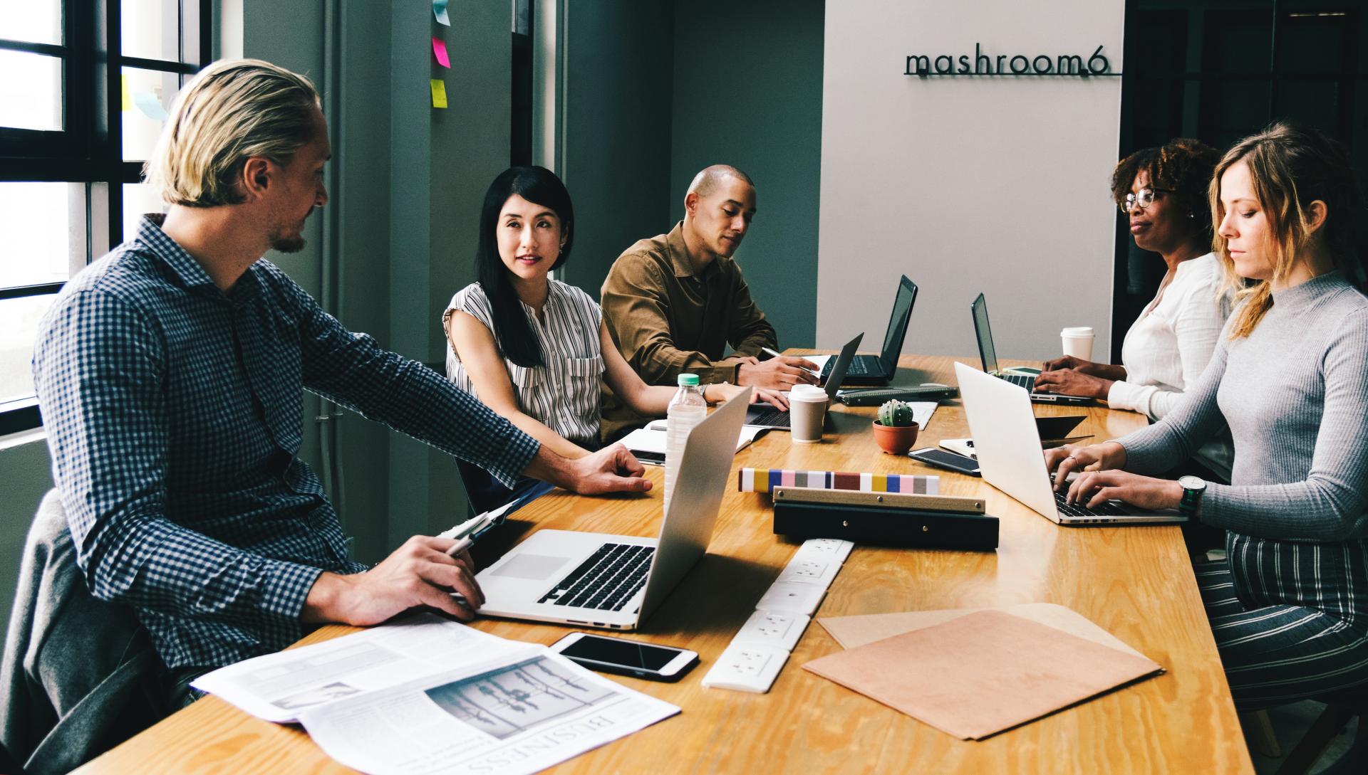 people sat around a table working together with laptops